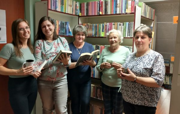 Bibliotekarz wraz z uczestniczkami spotkania na tle regałów z książkami