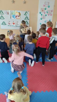 Bibliotekarka trzymająca w ręku książkę i pokazująca ją otaczającym ją dzieciom