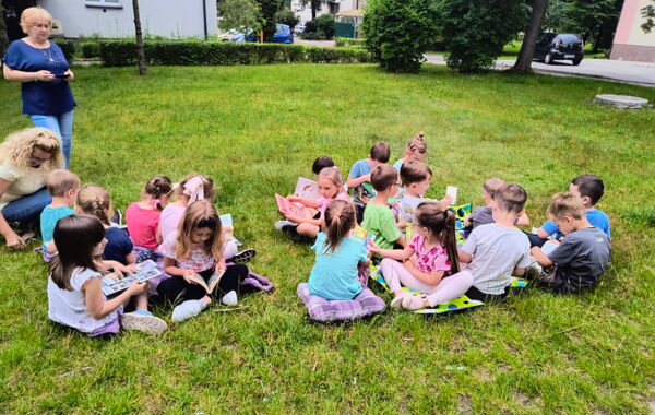 Dzieci siedzące na poduszkach na trawie czytające książki