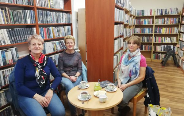 Trzy uczestniczki spotkania siedzące przy stoliku z kawą i słodkim dodatkiem