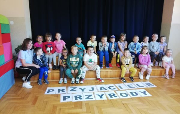 Przedszkolaki siedzące na schodkach. Obok nich ich wychowawczyni