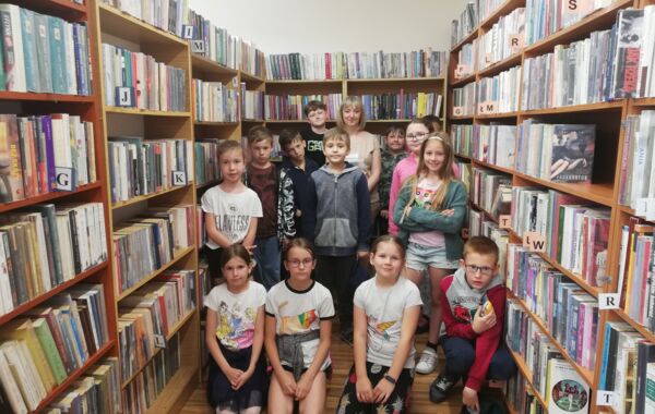 Uczniowie z klasy trzeciej wraz z bibliotekarzem na tle regałów z książkami