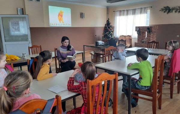 Bibliotekarz w trakcie odczytywania dzieciom książki o przygodach Kubusia Puchatka