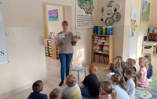 Bibliotekarka pokazująca siedzącym na dywanie przedszkolakom książeczki pt. „Babcia” i „Dziadek”