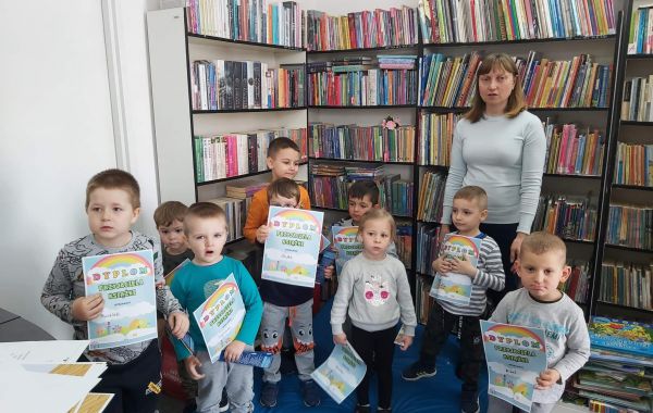 Dzieci trzymające dyplomy wraz z bibliotekarzem na tle regałów