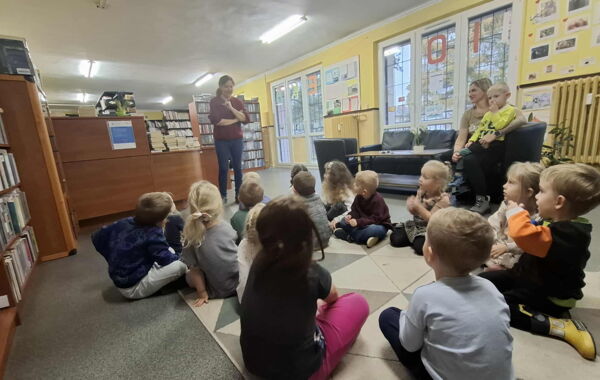 Bibliotekarka oraz dzieci biorące udział w lekcji bibliotecznej