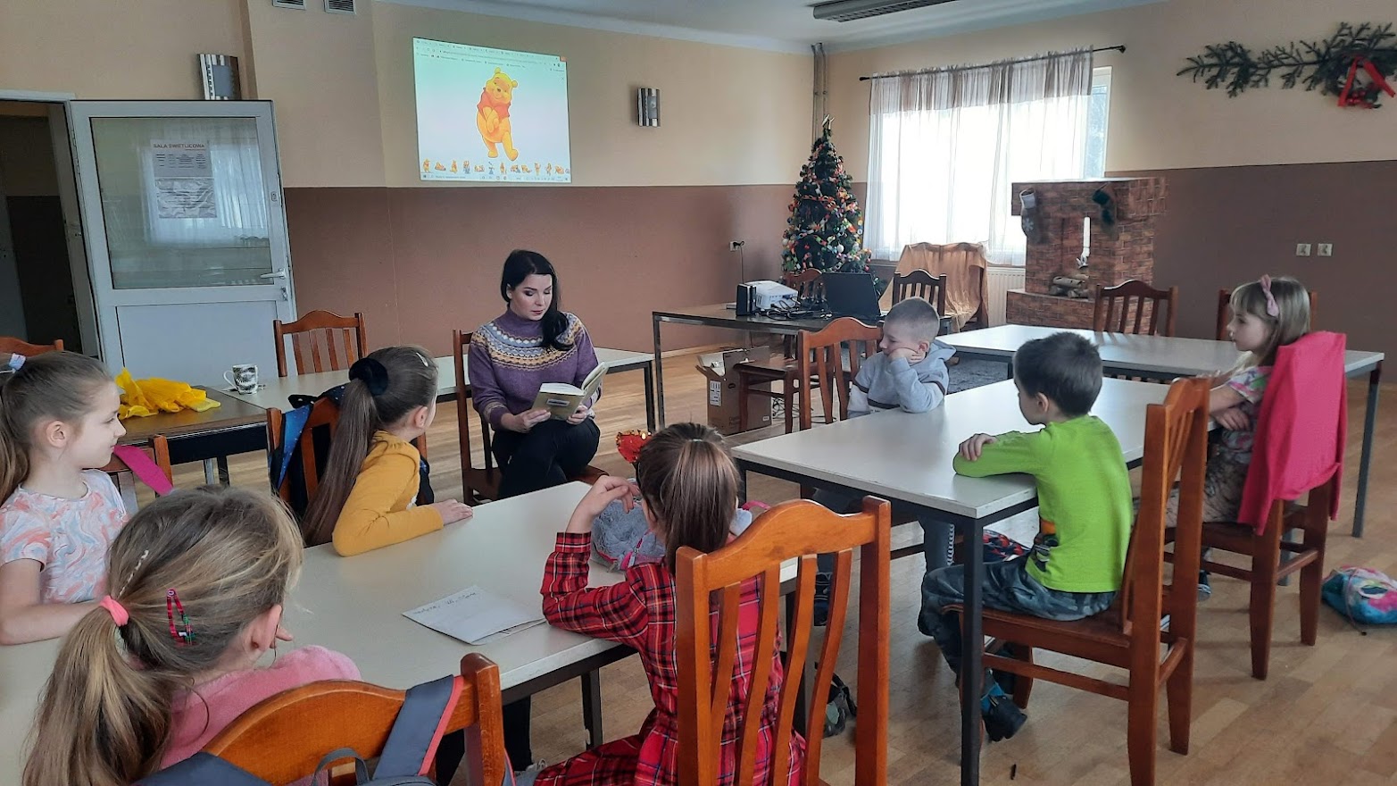 Bibliotekarz w trakcie odczytywania dzieciom książki o przygodach Kubusia Puchatka
